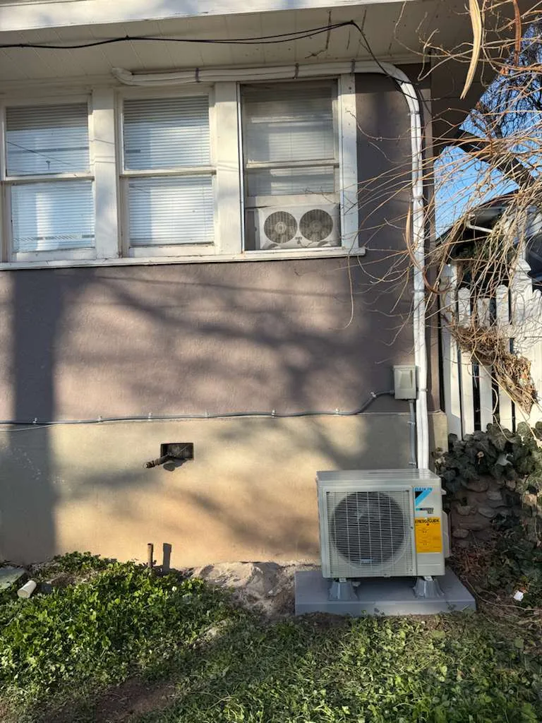 New Daikin mini-split outdoor unit installed at an older Salt Lake City home, with the old window AC still visible above
