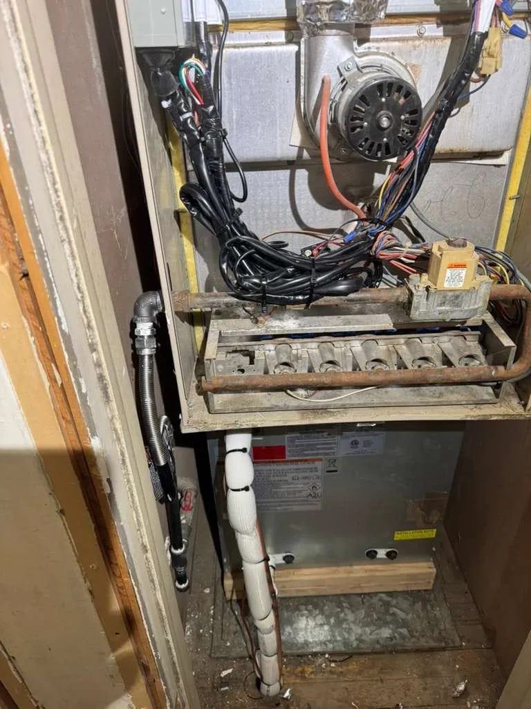 Furnace de flujo descendente abierto para reparación por Lucas Heating and Air, mostrando el motor inductor, los quemadores y la válvula de gas en un clóset de servicio