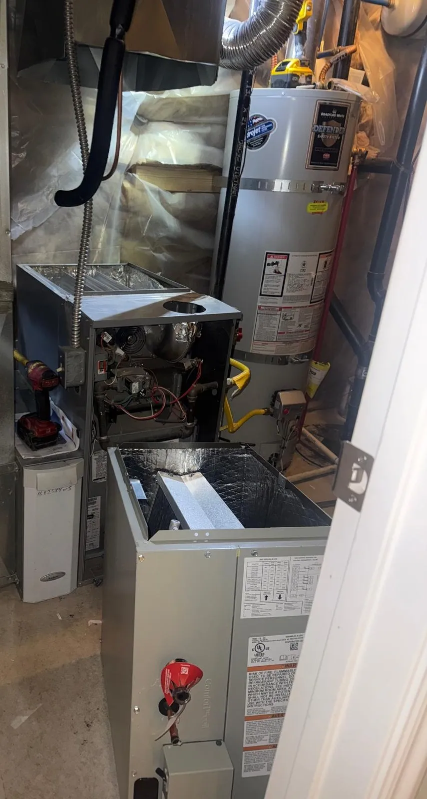 Furnace and AC replacement in progress in a West Valley City mechanical closet, old furnace opened with the new coil cabinet staged in front