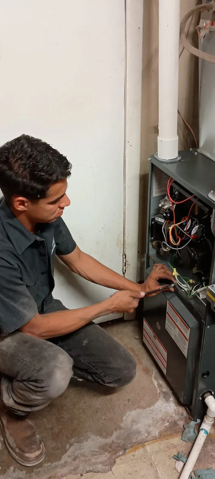 Lucas Heating and Air technician kneeling at an open furnace cabinet during a repair