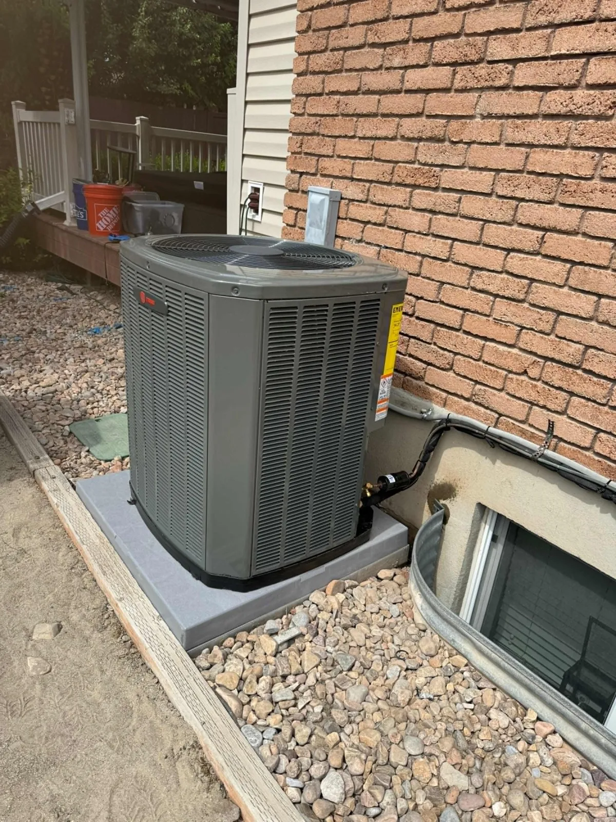 New Trane air conditioner condenser installed by Lucas Heating and Air on a pad in a rock bed beside a brick home